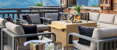 A wooden deck with outdoor seating, a table with glasses and a bottle, and a mountain view.