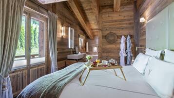 Une chambre dans un chalet en bois, avec un lit, un plateau de petit-déjeuner, un lavabo et une fenêtre avec des rideaux.
