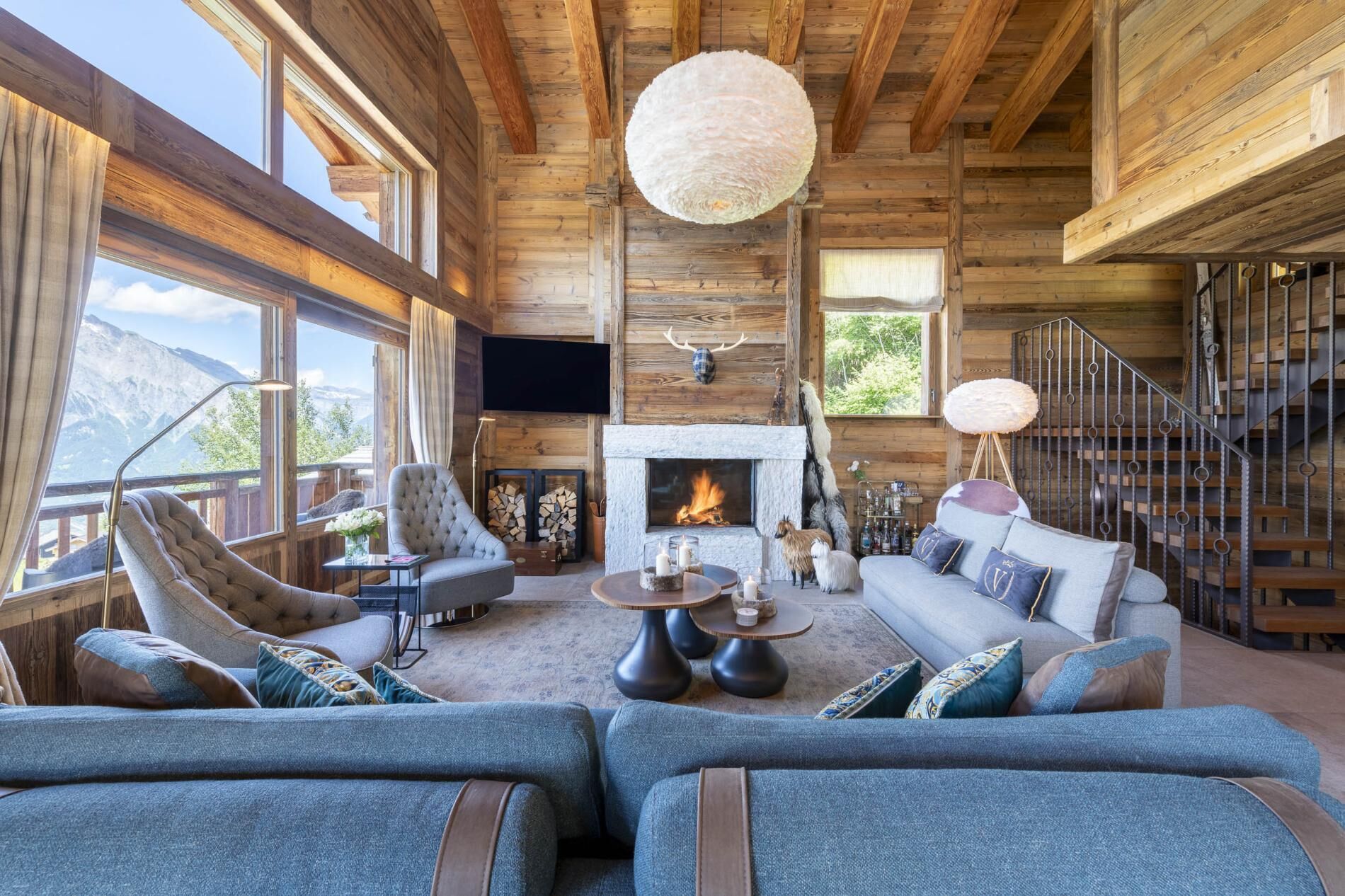 L’intérieur d’une cabane en rondins, avec une cheminée, un coin salon et un escalier.
