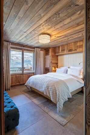 Une chambre aux murs lambrés, avec un lit, un banc et une vue sur les montagnes.