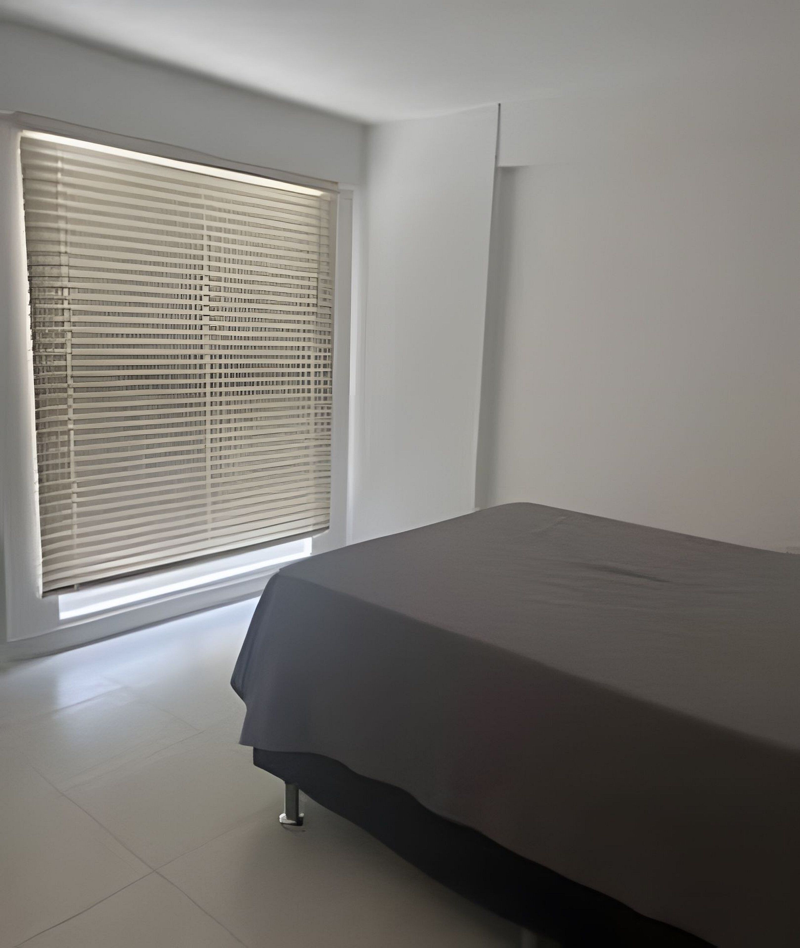 A bedroom with a bed, a window with blinds, and a white wall.