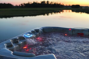 A hot tub with a control panel, surrounded by a calm body of water and a sunset in the background. - Timber Bear Lake House (New Lisbon)