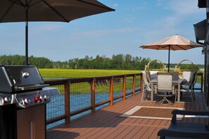 Une terrasse avec un barbecue, du mobilier d’extérieur et une vue sur un champ verdoyant.