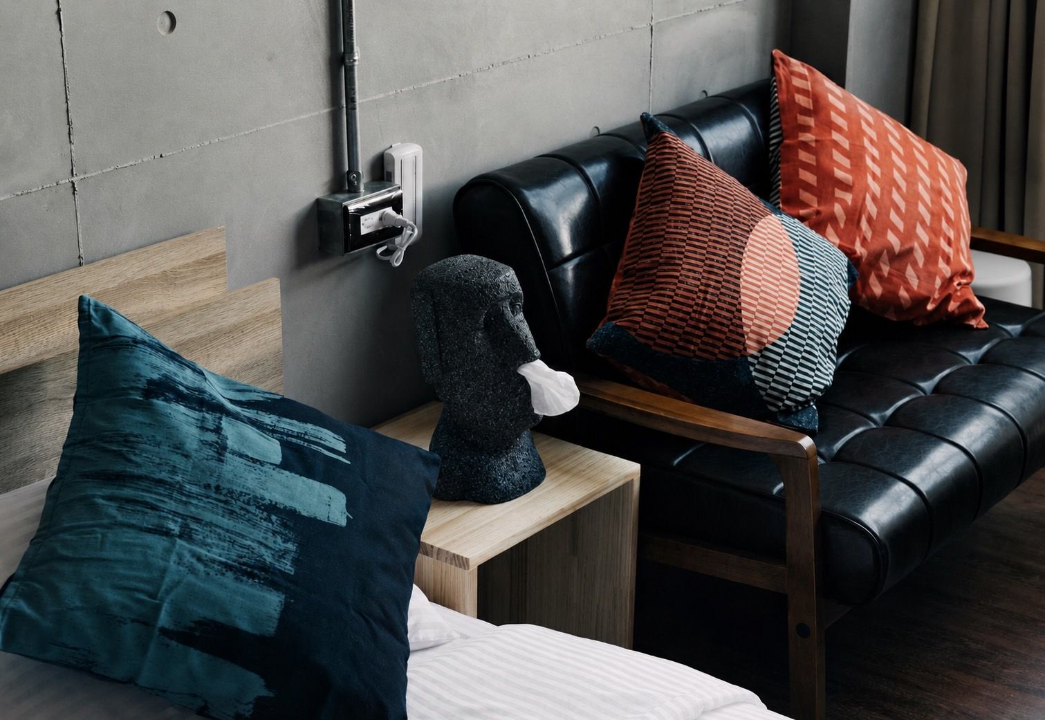 A modern room with a bed, a nightstand, a black leather sofa, and decorative pillows.