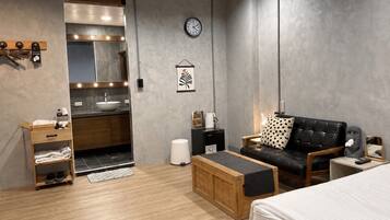A modern room with a bed, a sofa, a small table, a wooden cabinet, a sink, and a clock on the wall.