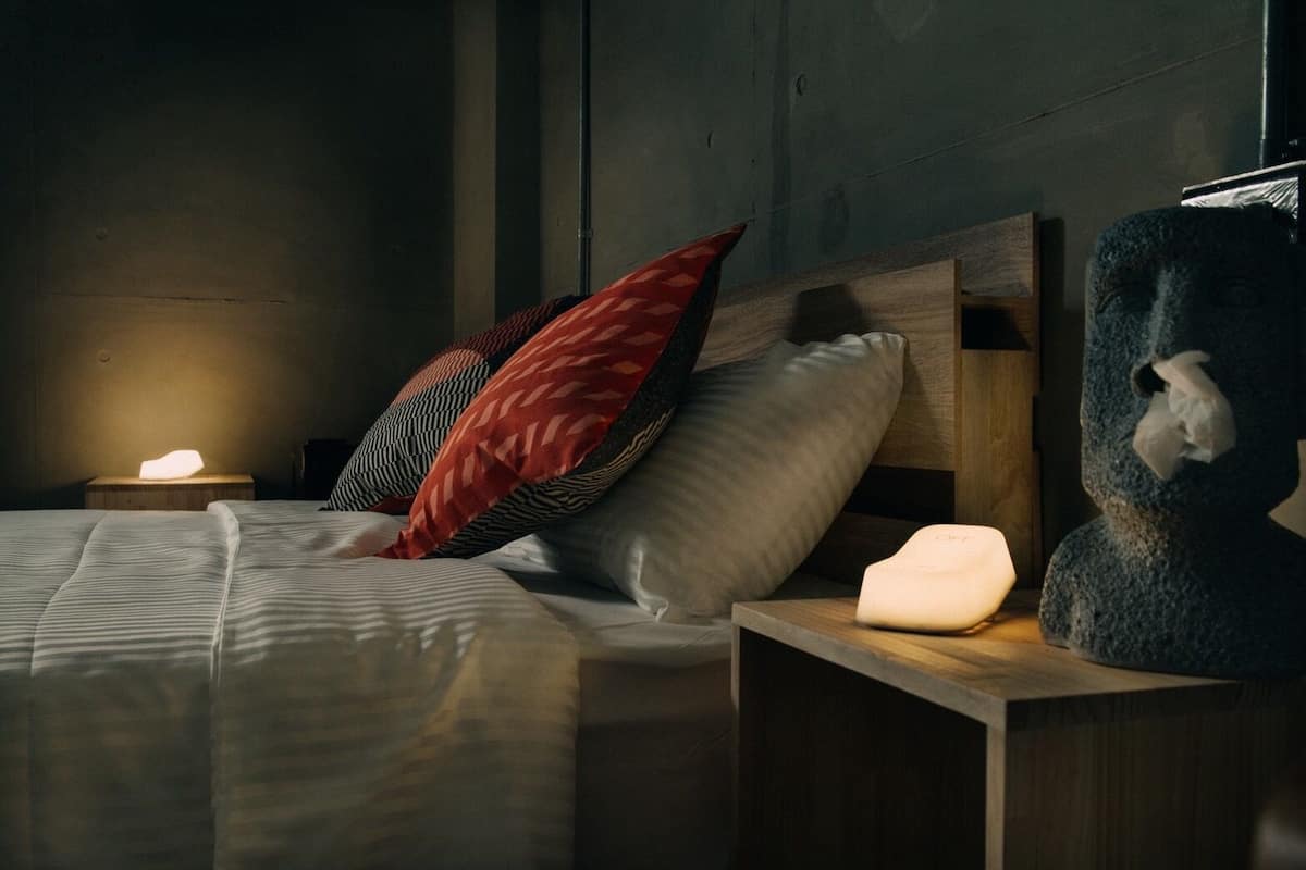 A bed with pillows, a bedside lamp, and a stone sculpture.