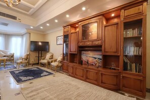 A living room with a large wooden entertainment center, a flat-screen TV, and a bookshelf. - New Cairo,vast classy 3 BR Apt.in quite villa inside fruity garden. Guarded 24/7 (New Cairo City)