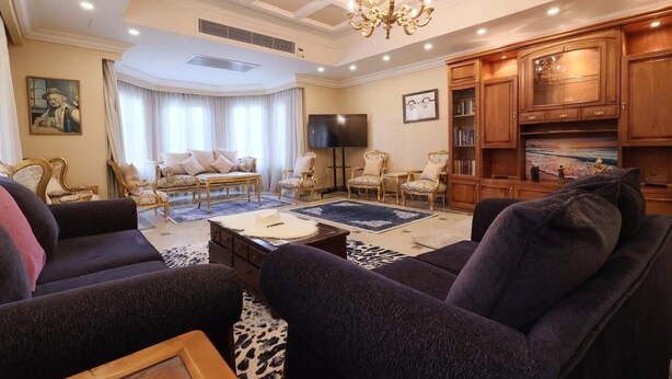 A spacious living room with a chandelier, multiple seating options, a flat-screen TV, and wooden cabinets. - New Cairo,vast classy 3 BR Apt.in quite villa inside fruity garden. Guarded 24/7 (New Cairo City)