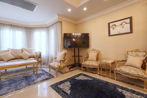 Un salón con un sofá, dos sillones, una mesa de centro, un televisor de pantalla plana y un cuadro en la pared.