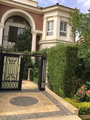 A gated entrance with a number '85' sign, a paved pathway, and a well-maintained hedge. - New Cairo,vast classy 3 BR Apt.in quite villa inside fruity garden. Guarded 24/7 (New Cairo City)