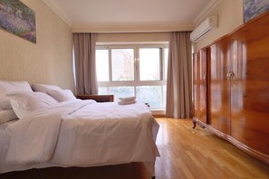 A bedroom with a bed, a window with curtains, a wooden wardrobe, and a painting on the wall. - New Cairo,vast classy 3 BR Apt.in quite villa inside fruity garden. Guarded 24/7 (New Cairo City)