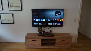 Ein Flachbildfernseher an der Wand über einem Holz-TV-Schrank mit Fernbedienung und Dekorationselementen.
