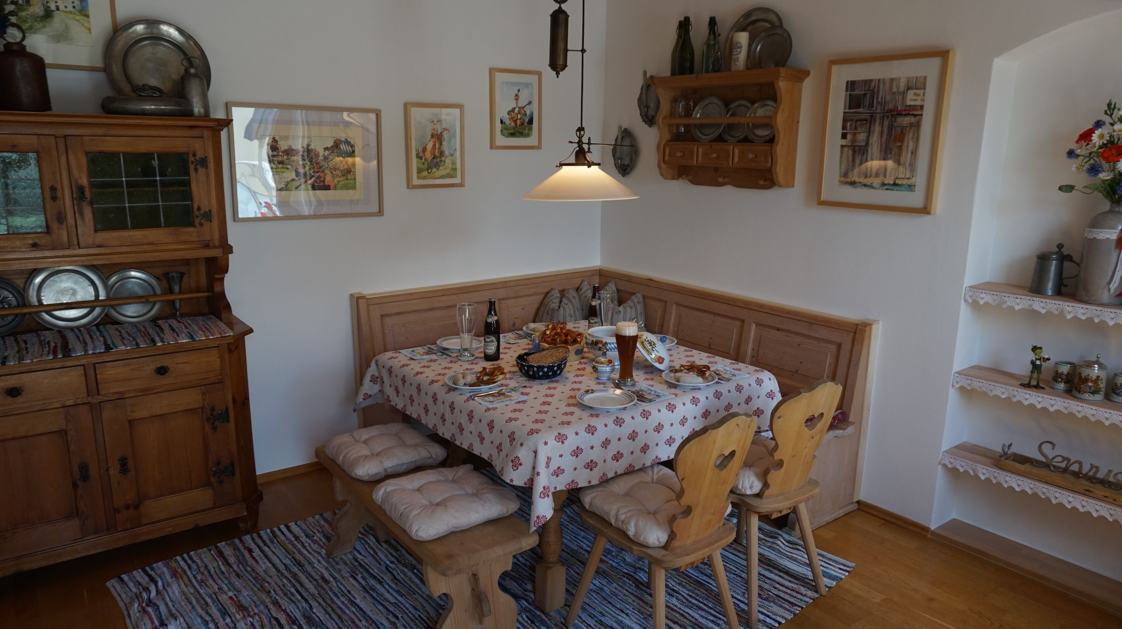 Ein Essbereich mit einem Holztisch, Stühlen, einer Bank und einer Tischdecke mit Muster.