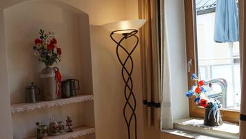 Ein gemütliches Zimmer mit Holzboden, einer Stehlampe, einem Fenster mit Vorhängen, einem Regal mit Dekoration und einem Sessel mit Tisch.