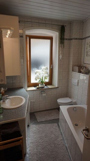 Ein Badezimmer mit Fenster, Waschbecken, Toilette und Badewanne.