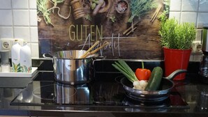 Eine Küche mit einer Edelstahl-Dunstabzugshaube, einer Holz-Spritzschutzwand mit dem Schriftzug 'GUTEN' sowie verschiedenen Küchenutensilien und frischem Obst und Gemüse auf der Arbeitsfläche.