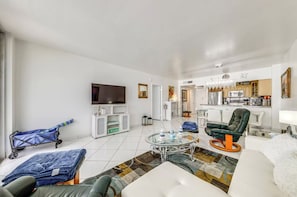 A modern living room with a flat-screen TV, a sofa, a coffee table, and a kitchen in the background. - Beachfront Condo, Sleeps 6, Pool & Beach Access (Hollywood)
