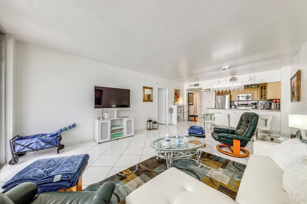 A modern living room with a flat-screen TV, a sofa, a coffee table, and a kitchen in the background. - Beachfront Condo, Sleeps 6, Pool & Beach Access (Hollywood)