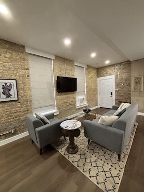 A living room with a fireplace, a flat-screen TV mounted on the wall, and a sofa with cushions.