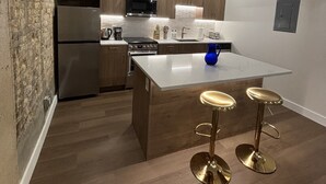 Una cocina moderna con armarios de madera, electrodomésticos de acero inoxidable, una isla central con taburetes e iluminación colgante.