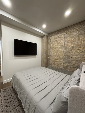 A bedroom with a bed, a mounted TV, a stone wall, and a door.