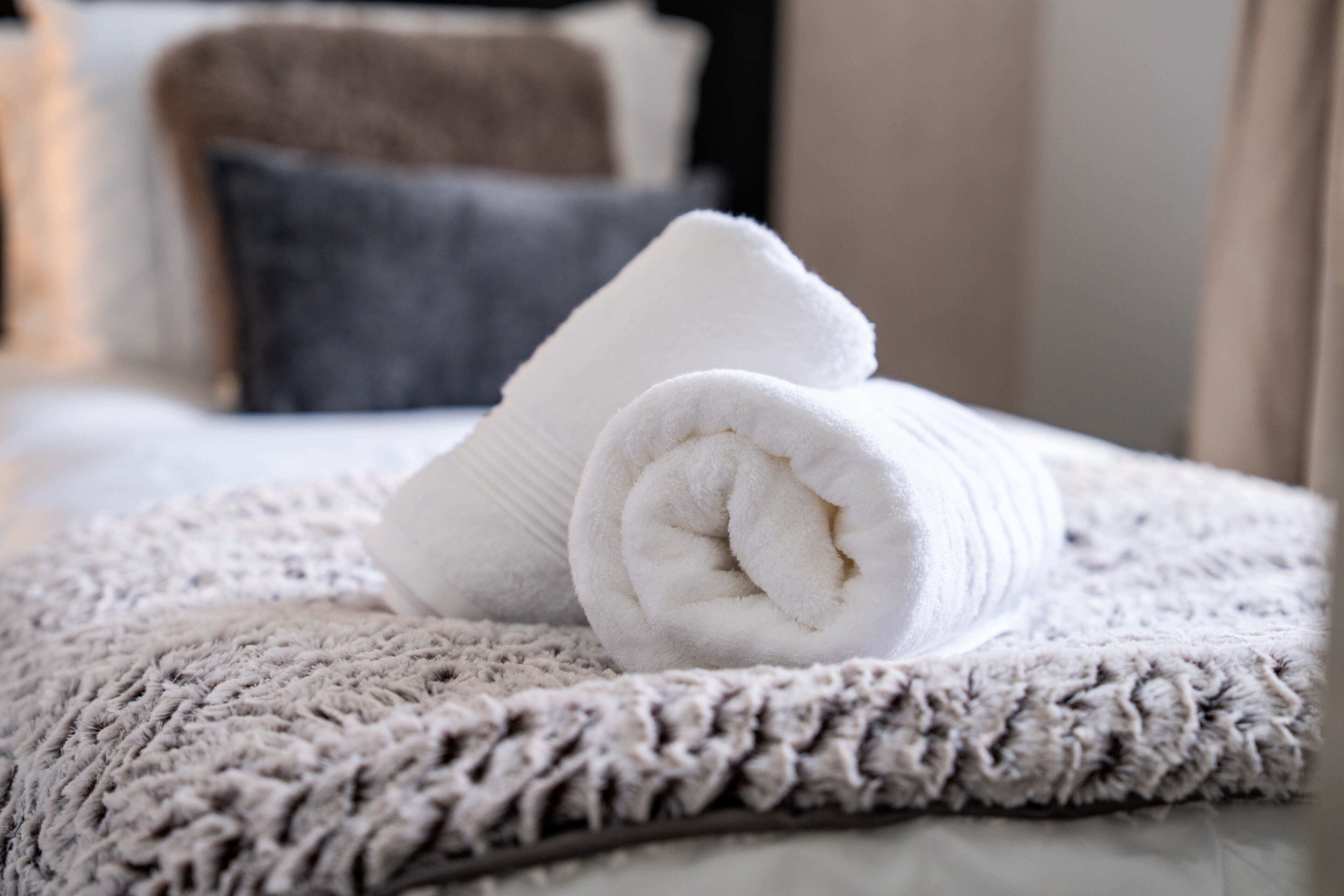 En prydligt vikt, vit handduk på en mönstrad, beige matta, en mörkbrun kudde och en vit kudde i ett hotellrum.