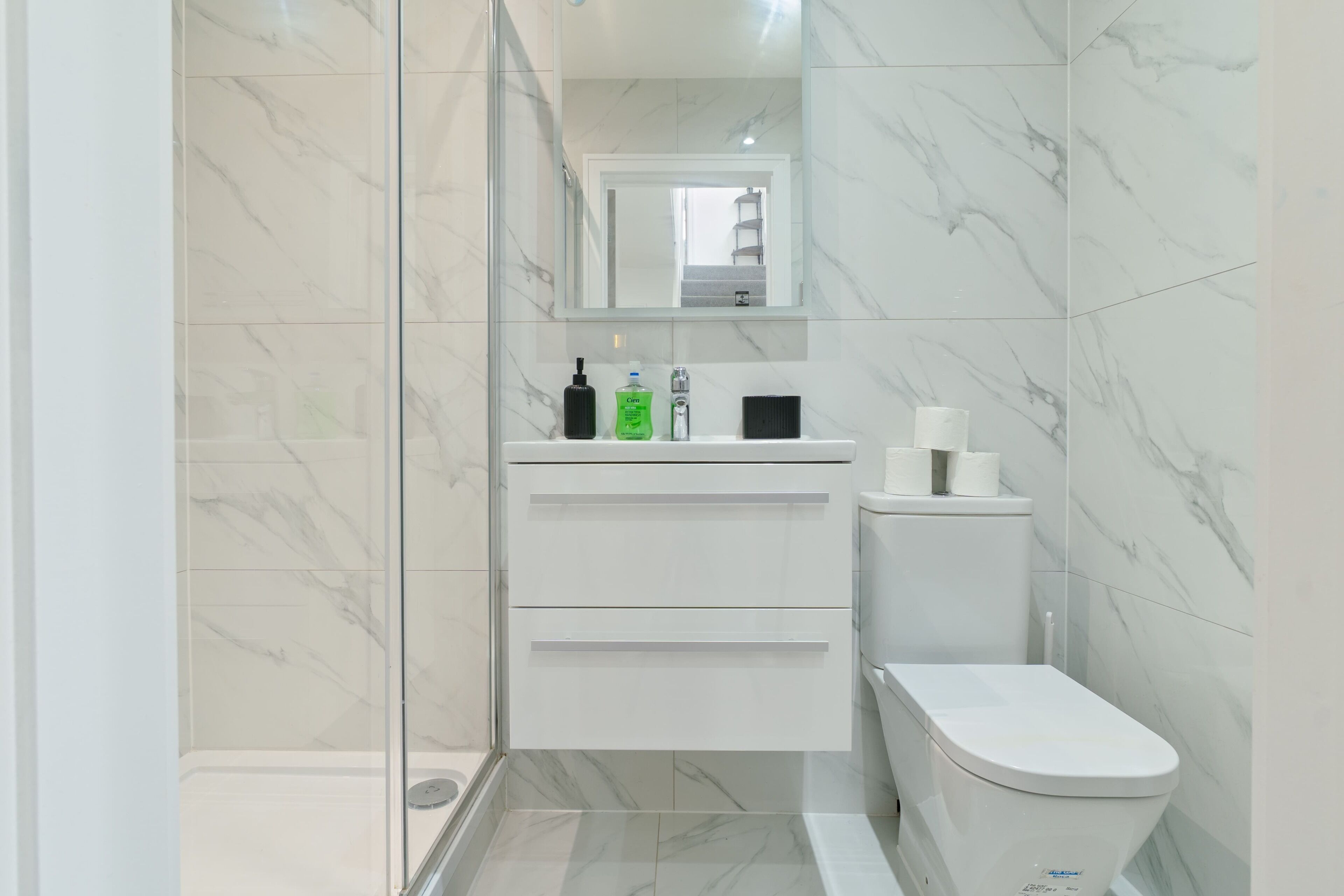 Ein modernes Badezimmer mit Duschkabine aus Glas, einer weißen Toilette und einem Waschtisch mit Pflegeprodukten.