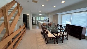Un comedor amplio con una mesa grande y sillas, una cocina al fondo y una escalera de madera.