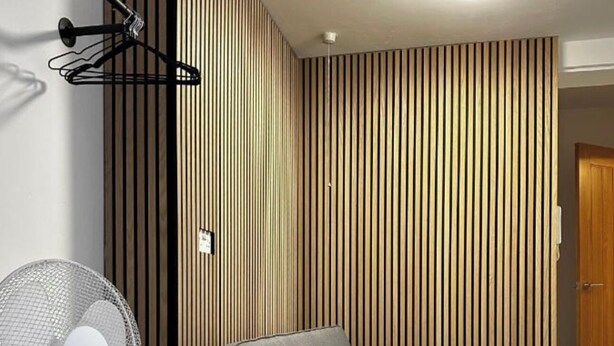 Una camera moderna con un divano, una ventola a piantana, una parete con listelli di legno e una porta.