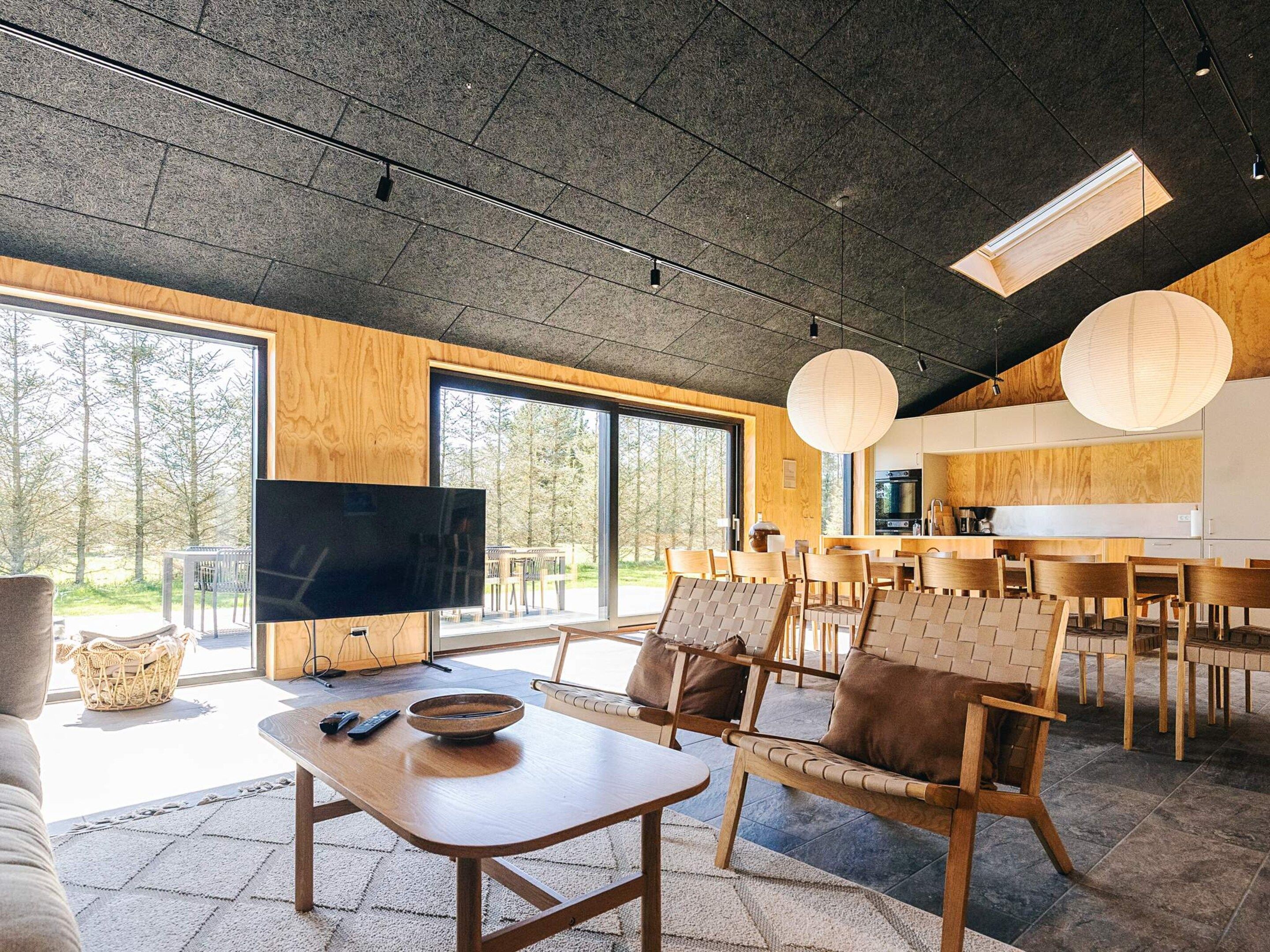 A modern living room with a large flat-screen TV, wooden furniture, and a view of the outdoors.