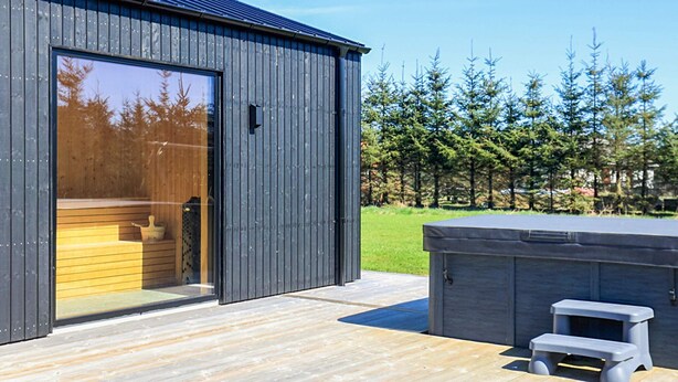 A modern building with a large glass door, a wooden deck, and a hot tub. - 5 Star Holiday Home in Saeby (Sæby)