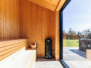 A wooden interior with a sauna, a bench, and a view of a playground outside. - 5 Star Holiday Home in Saeby (Sæby)