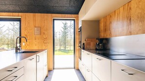 A modern kitchen with wooden cabinetry, a black countertop, and a view of trees outside. - 5 Star Holiday Home in Saeby (Sæby)