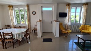 A room with a dining table, chairs, a TV, a yellow armchair, and a door leading to another room.