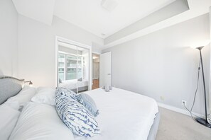 Ein Schlafzimmer mit einem großen Bett, einem Nachttisch, einer Stehlampe und einem Fenster.