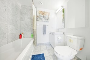 A bathroom with a bathtub, toilet, sink, and a painting on the wall. - Upscale 3BR/2BA | Cold Plunge · Sauna · Steam | Parking | Downtown Toronto (Toronto)