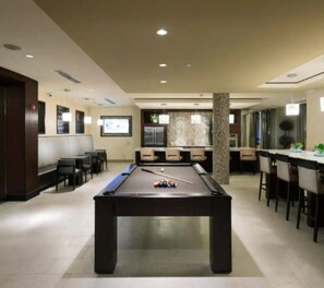 Une table de billard dans une pièce bien éclairée, avec des sièges et un coin bar.