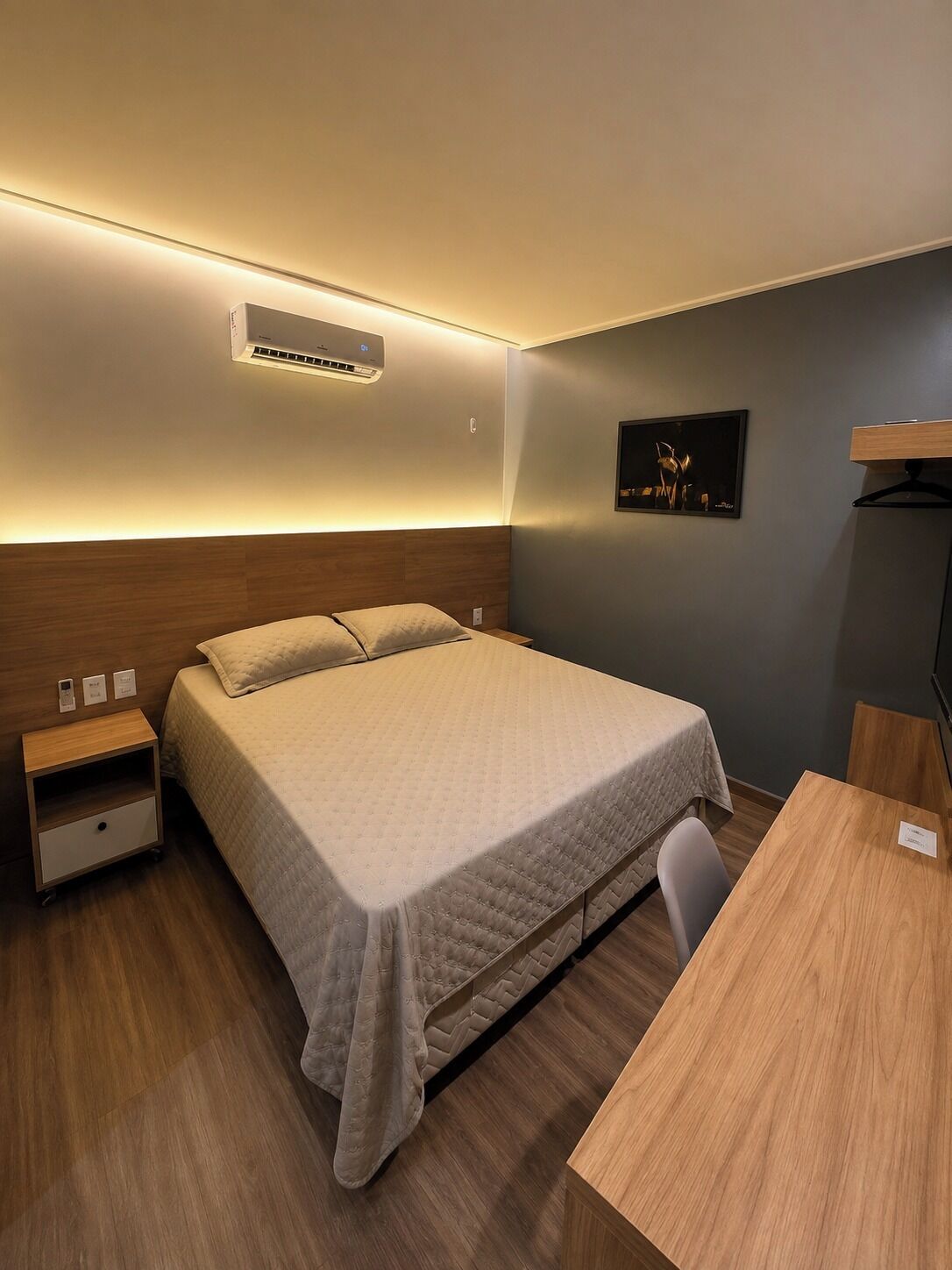 A hotel room with a bed, bedside table, and a desk with a chair.