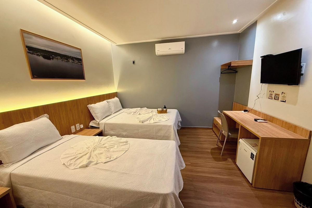 A hotel room with two beds, a desk, a TV, and a small kitchenette.