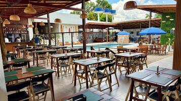 An outdoor dining area with tables and chairs, a pool, and umbrellas.
