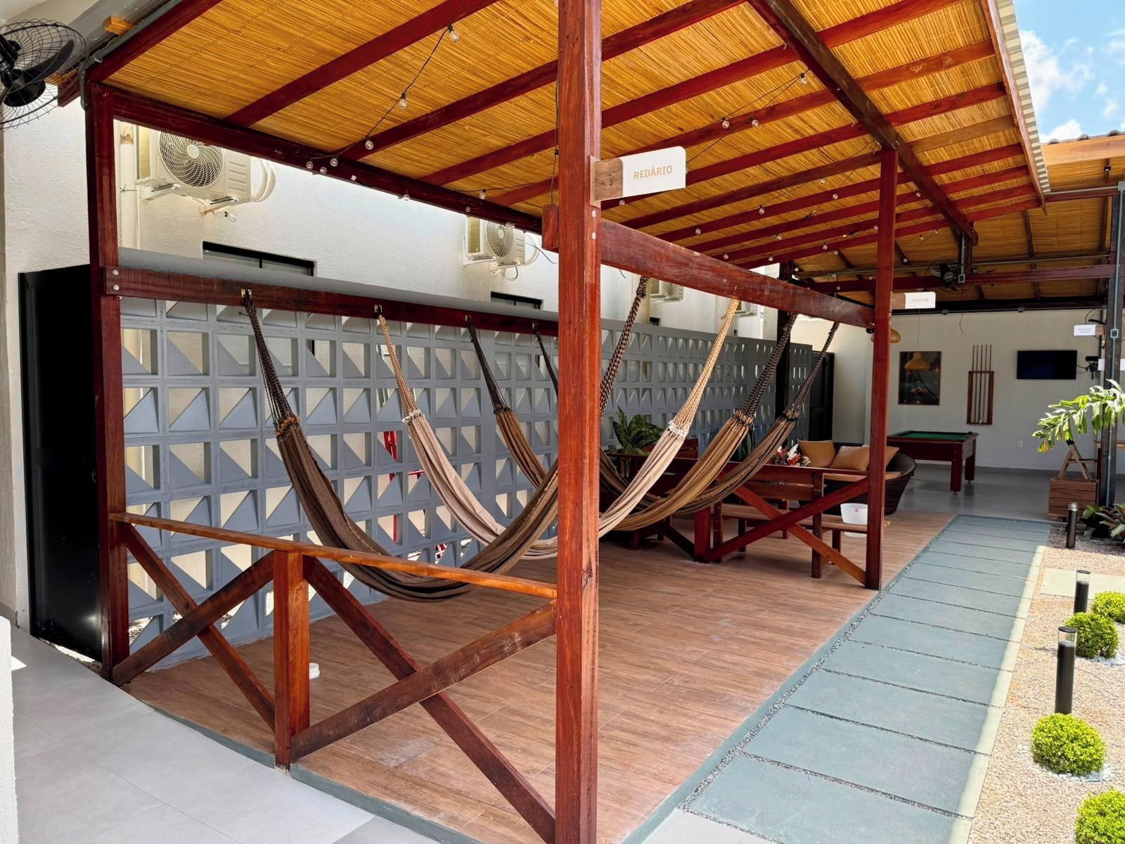 Un espacio de estar al aire libre cubierto con vigas de madera y techo de paja, que incluye varias hamacas y una mesa de billar.