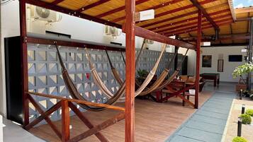 Un espacio de estar al aire libre cubierto con vigas de madera y techo de paja, que incluye varias hamacas y una mesa de billar.