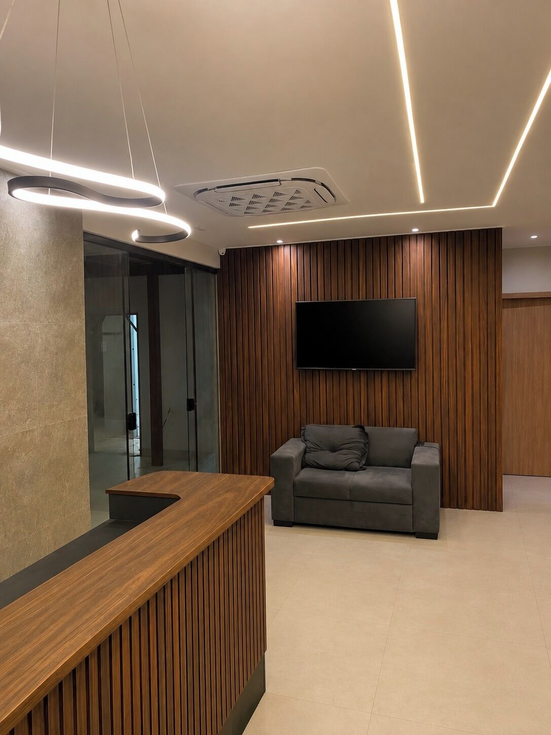 A reception area with a wooden reception desk, a grey sofa, and a mounted television.