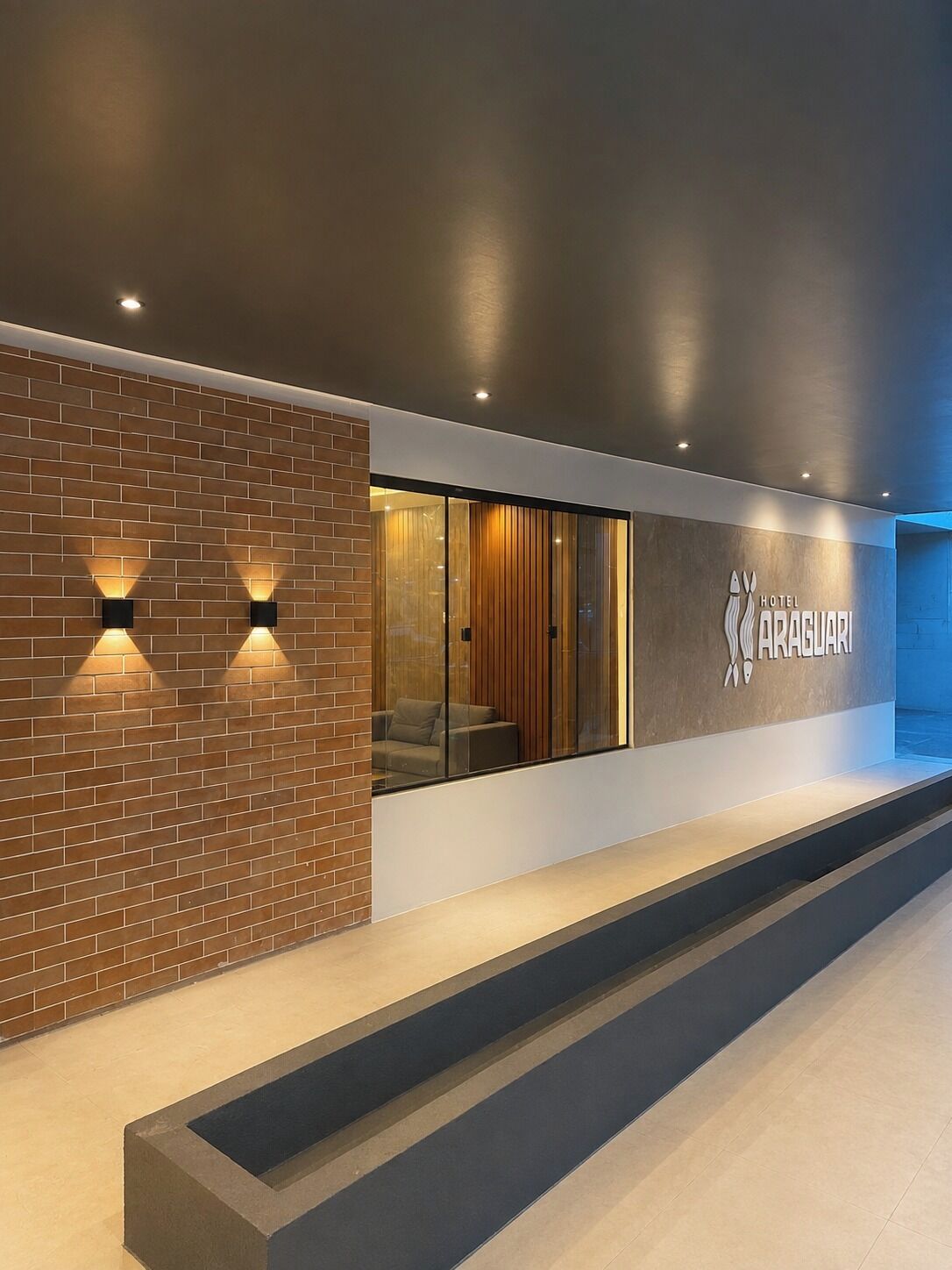A modern hotel lobby with a brick wall, a glass partition, and a seating area.