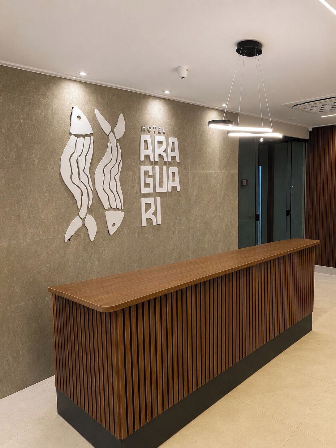 A hotel reception desk with a modern design, a wall-mounted sign with the hotel's name, and a ceiling-mounted light fixture.