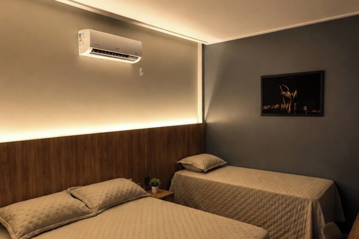 Habitación de hotel con dos camas, aire acondicionado de pared y una mesita con una planta.