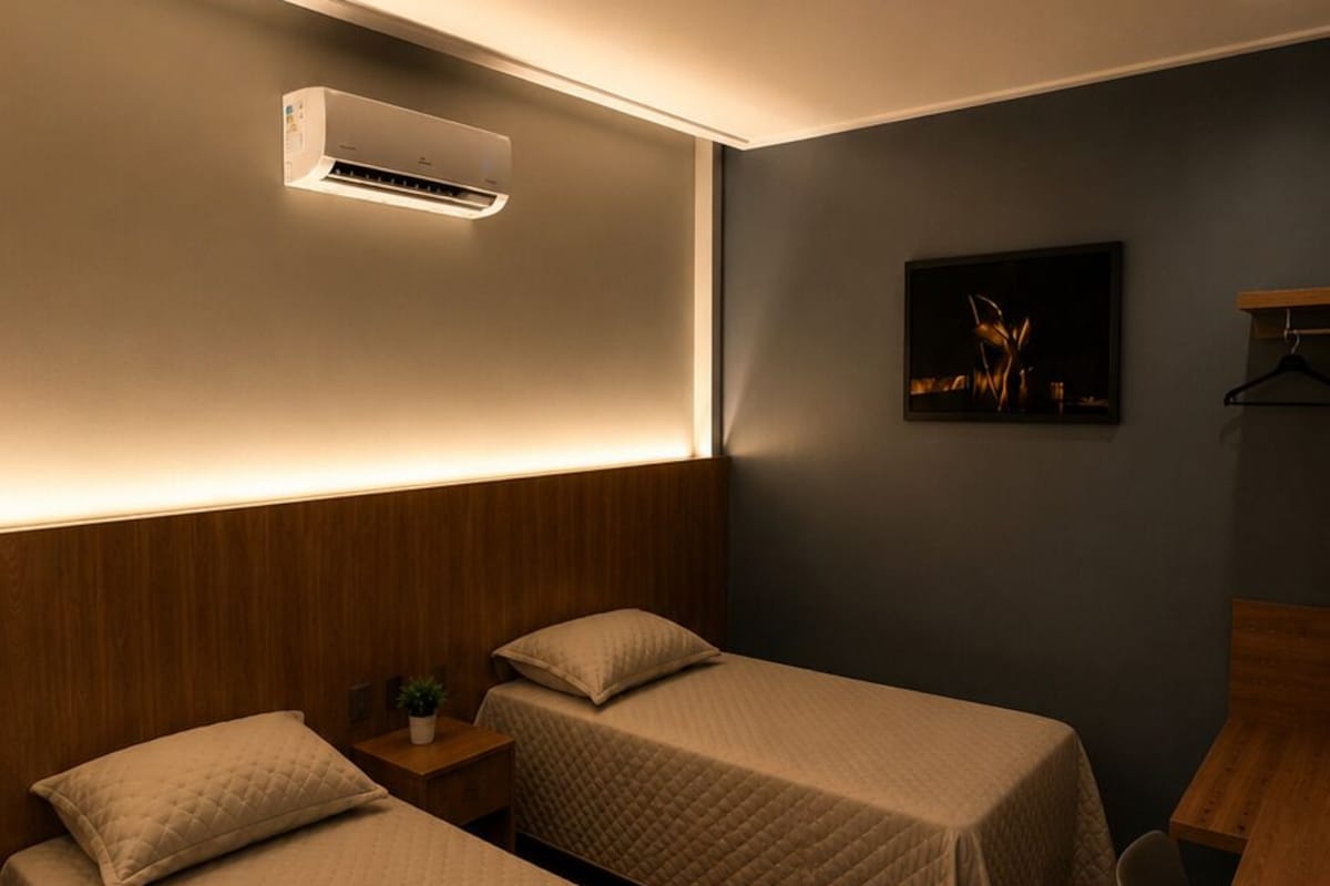 Habitación de hotel con dos camas, un escritorio, una planta colgante y aire acondicionado instalado en la pared.