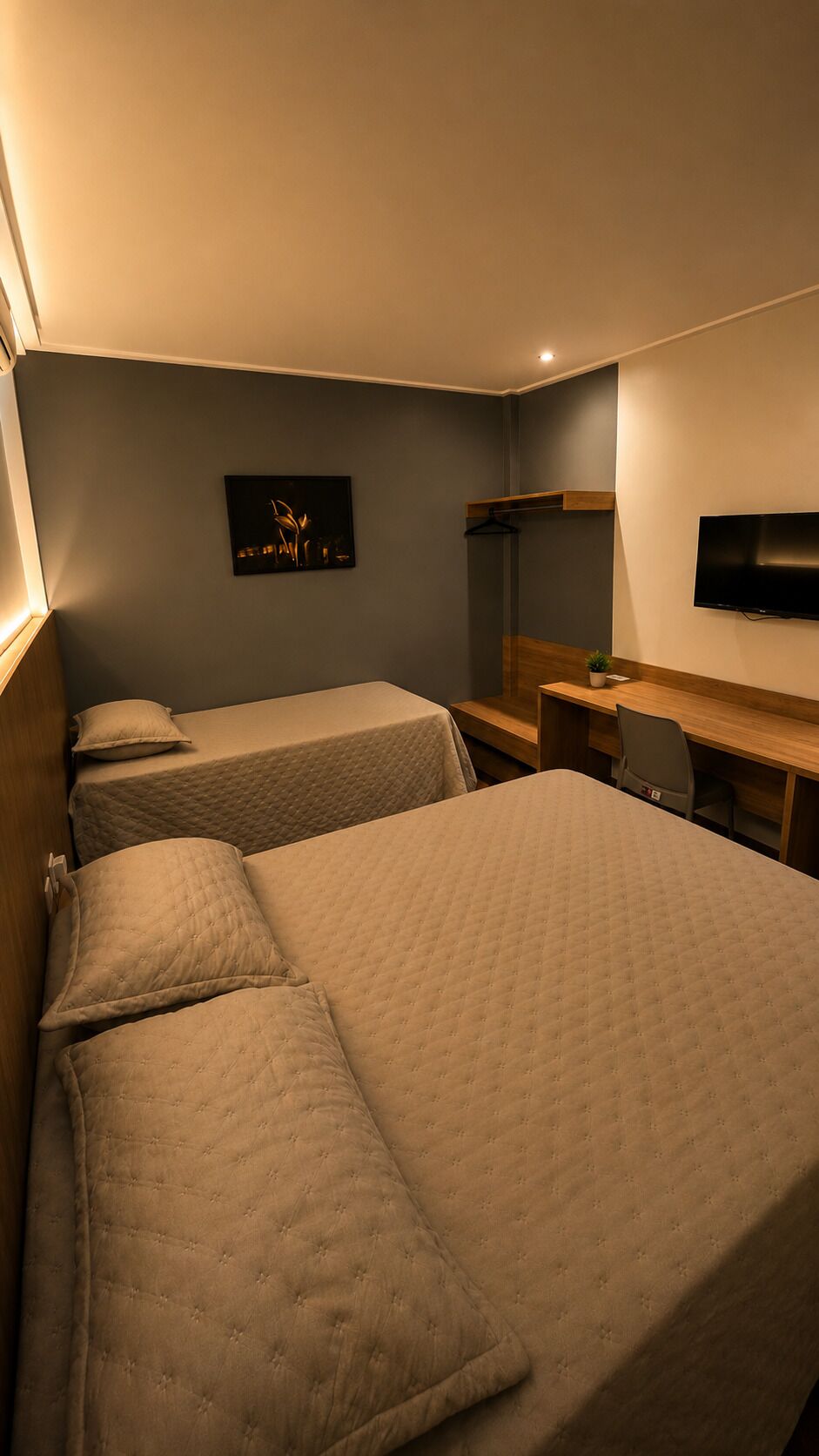 A hotel room with two beds, a desk, a chair, a TV, and a wall-mounted shelf.