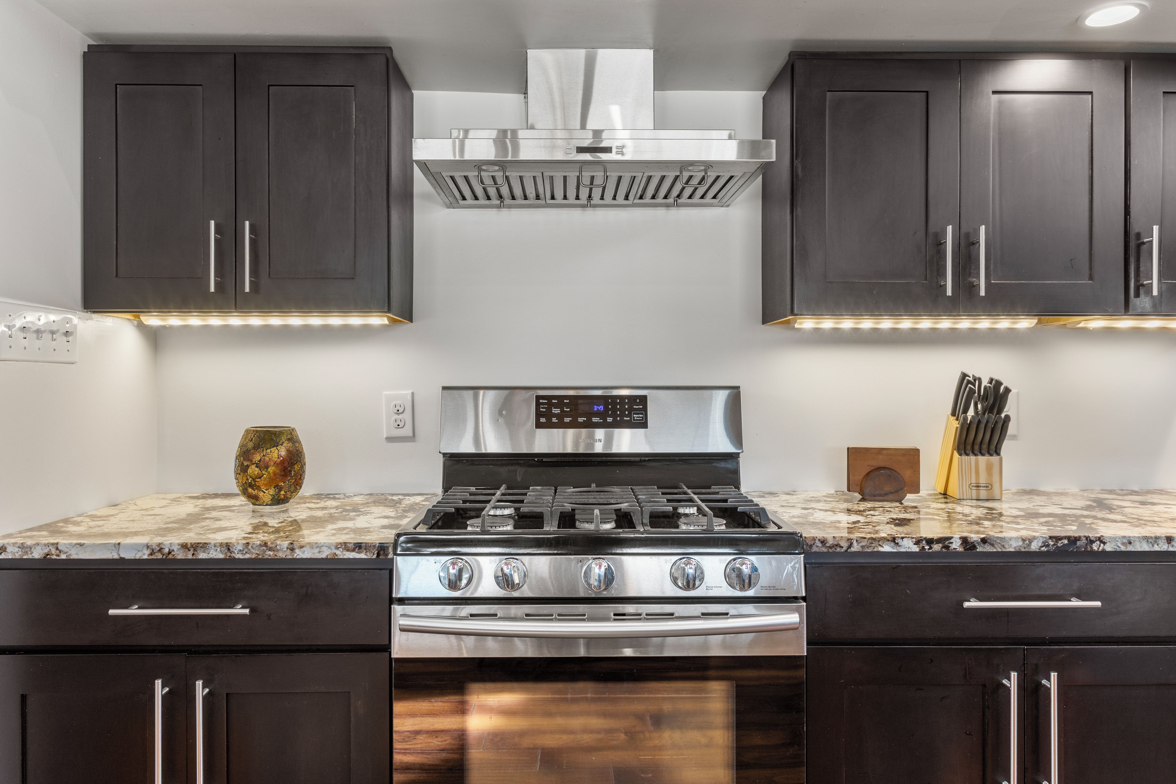A kitchen with dark cabinets, stainless steel appliances, and a marble countertop.