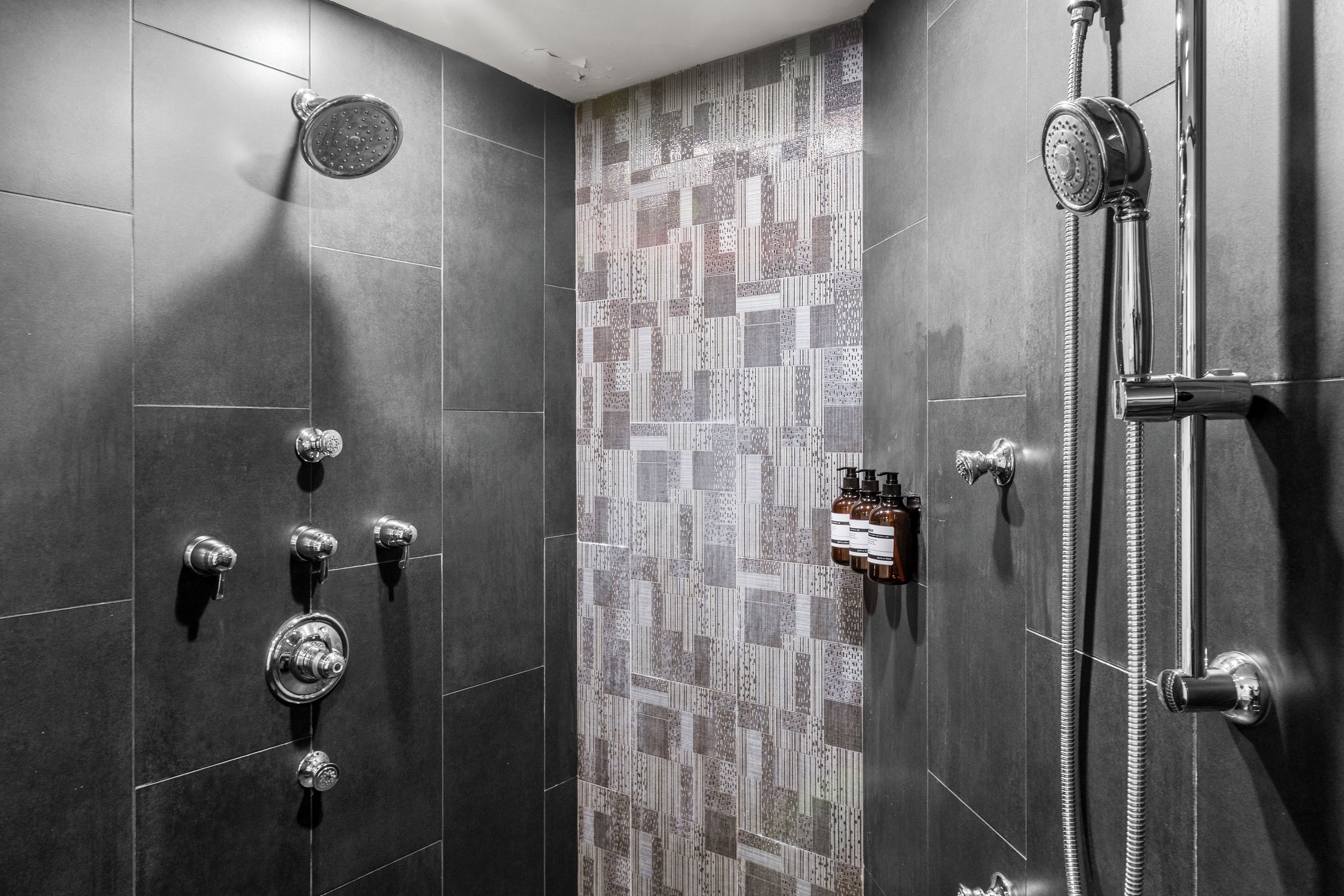 A shower with multiple controls, a handheld showerhead, and a wall-mounted faucet.